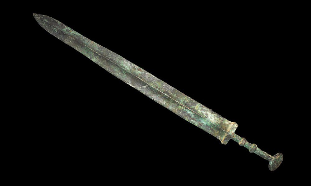 Chinese Han Dynasty Bronze Sword: Han Dynasty, 206 BC-220 AD. A Han Dynasty style sword, the blade waisted with central rib; the guard elliptical in section with thin ribbed round-section grip and dished disc pommel. UK art market, ac