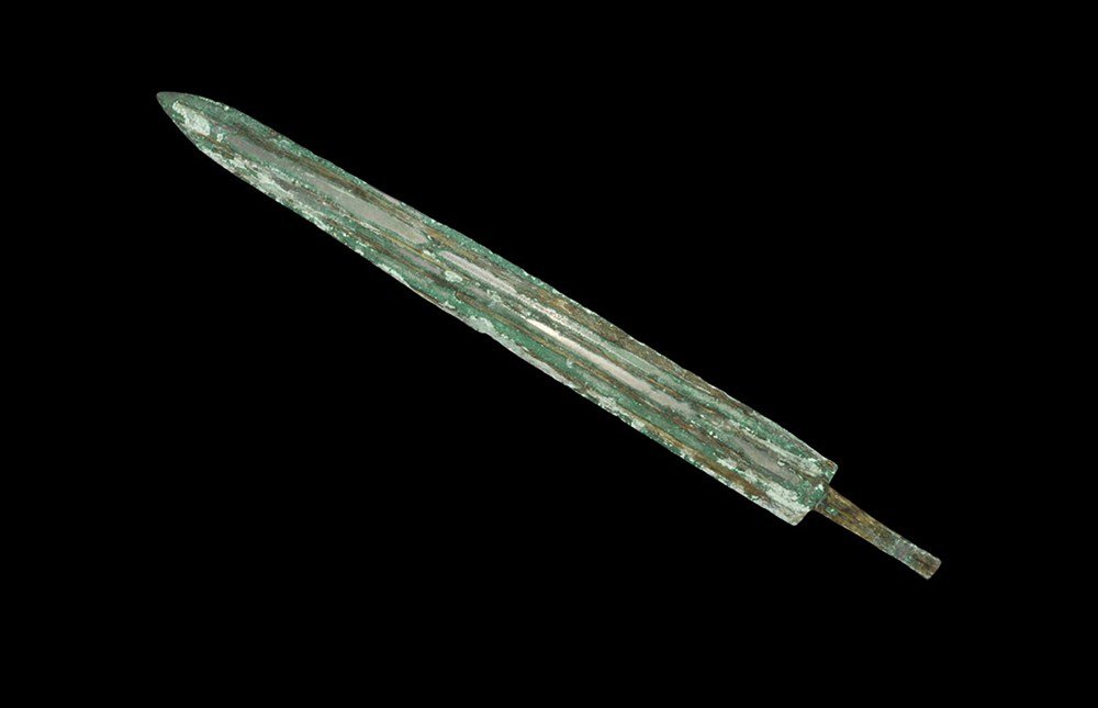 Chinese Zhou Bronze Sword Blade: Zhou Dynasty 1046–256 BC. A cast bronze short sword blade with central midrib and tapering profile; the tang rectangular-section and grip absent; the blade and tang with fragments of wood adhering t