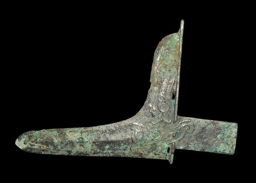 Chinese Bronze Zhou Period Halberd: Zhou Dynasty 1046–256 BC. A cast bronze halberd with rectagular tang and L-shaped blade; the blade and tang with low relief zoomorphic designs, characters to one face. UK art market, acquired prior 