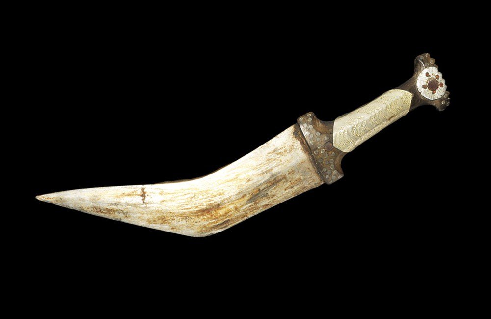 Middle Eastern Steel Janbiyya Dagger: Omani, 19th century AD. A dagger comprising a lentoid-section blade and carved wooden grip; the triangular blade with curved profile, the grip T-shaped with lozengiform sleeve and discoid plate with e