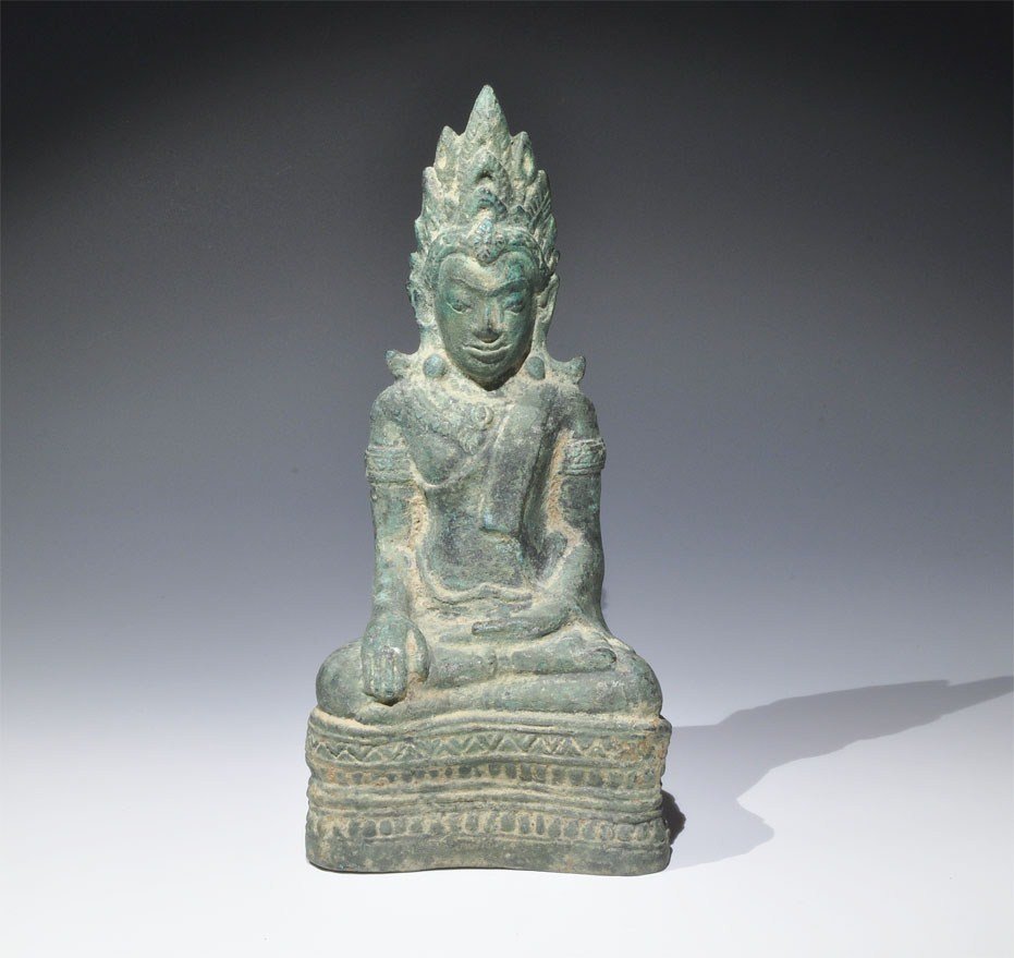Cambodian Bronze Seated Buddha Figurine: Circa 17th century AD. A finely modelled figurine depicting a cross-legged Buddha on a decorated plinth, the left hand resting in the lap and the right hand on the knee; the body robed and head crowne