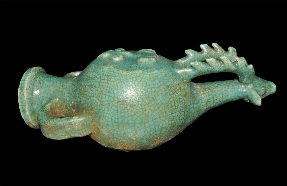 Islamic Ceramic Zoomorphic Rhyton: An undated ceramic Raqqa-ware archaistic rhyton with animal-head finial, globular body, two strap handles to funicular neck with everted rim; to the upper face a raised design of a human facing bust i