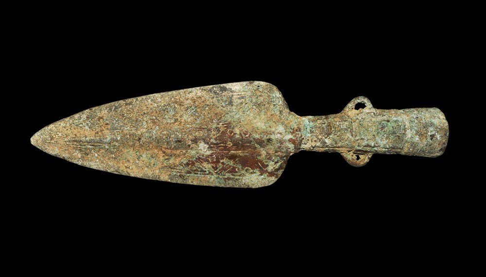 Chinese Style Bronze Spear Head: An undated cast archaistic spearhead comprising a leaf-shaped blade with incised pattern and central conical shaft with two attachment loops; the shaft with vertical bands of geometric ornament; the m