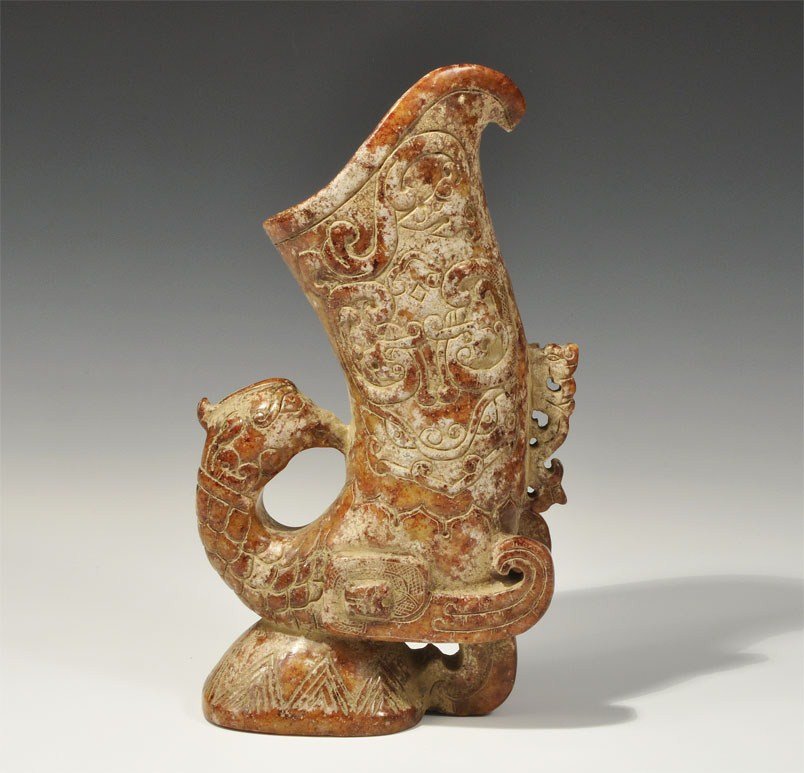 Chinese Style Stone Bird Vessel: An undated archaistic carved vessel with curved spout and conical foot; the body of the vessel formed as the recurved neck and body of a bird with beak resting on its back, wings projecting below; the