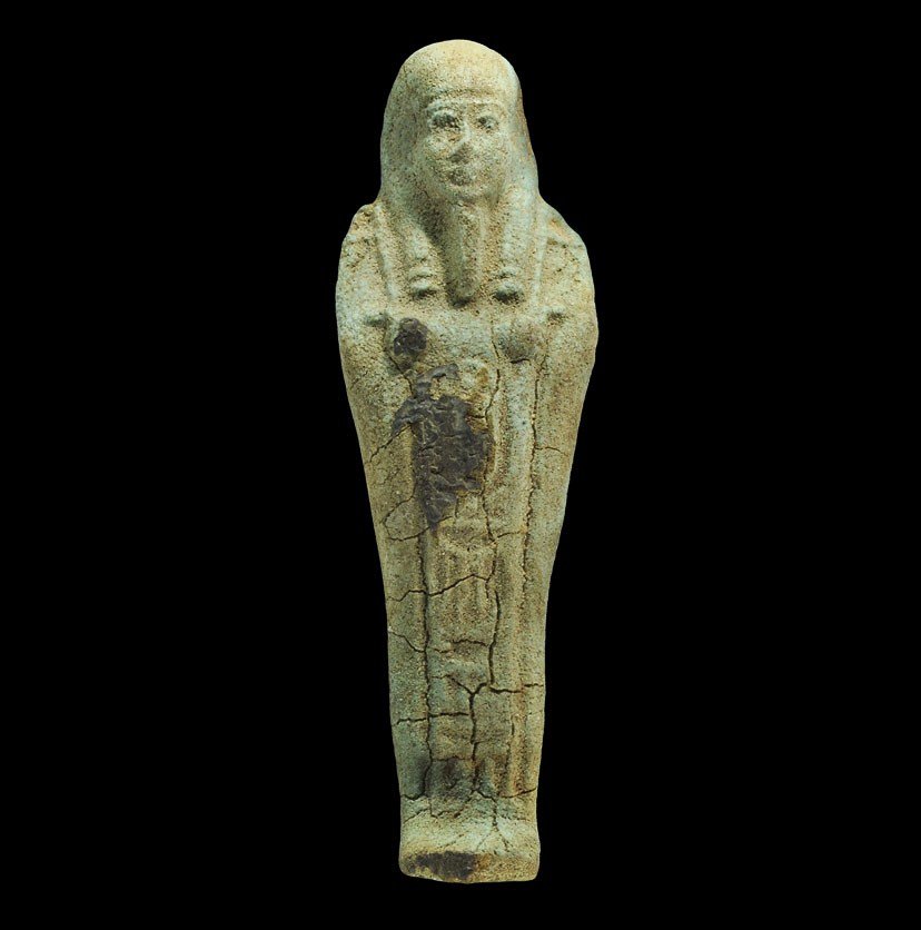 Egyptian Style Faience Shabti Figurine: A green glazed composition shabti figurine with hands at the chest, tripartite wig and plaited beard, probably a souvenier of the Grand Tour; old dealer's label to the reverse. 86 grams, 13.5 cm (5 1/