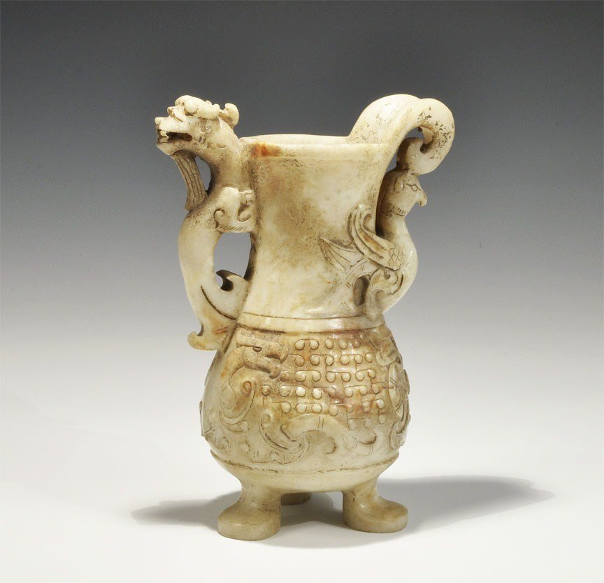 Chinese Style Onyx Bird Jug: An undated archaistic carved jug with squat body and tripod legs; to the neck a bird supporting the scrolled spout; the handle a dragon's head; to the body a frieze of stylised birds. 993 grams, 18 cm