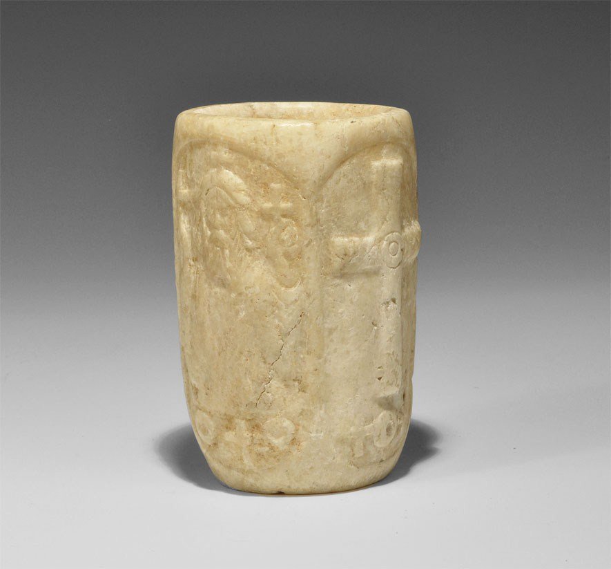 Byzantine Style Alabaster Nimbate Figural Beaker: An undated archaistic carved figural vessel in 5th-10th century AD style, with flat base and four elliptical panels to the side: two with low-relief cross motifs; one with bearded figure in three-quar