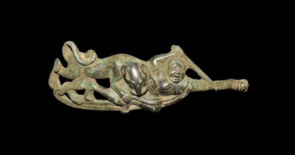 Chinese Style Bronze Dress Fastener: An undated archaistic Han Dynasty style fastener formed as a scene of a sword-wielding running man attacked by a jaguar, his left arm extended to form an animal-headed hook; to the underside, a discoi