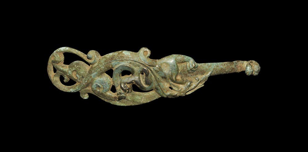 Chinese Style Bronze Dress Fastener: An undated archaistic Han Dynasty style fastener formed as a lupine with gaping mouth amid swirls and scrolled vegetation, at the upper end a recurved beast-head hook; to the underside, a discoid stud