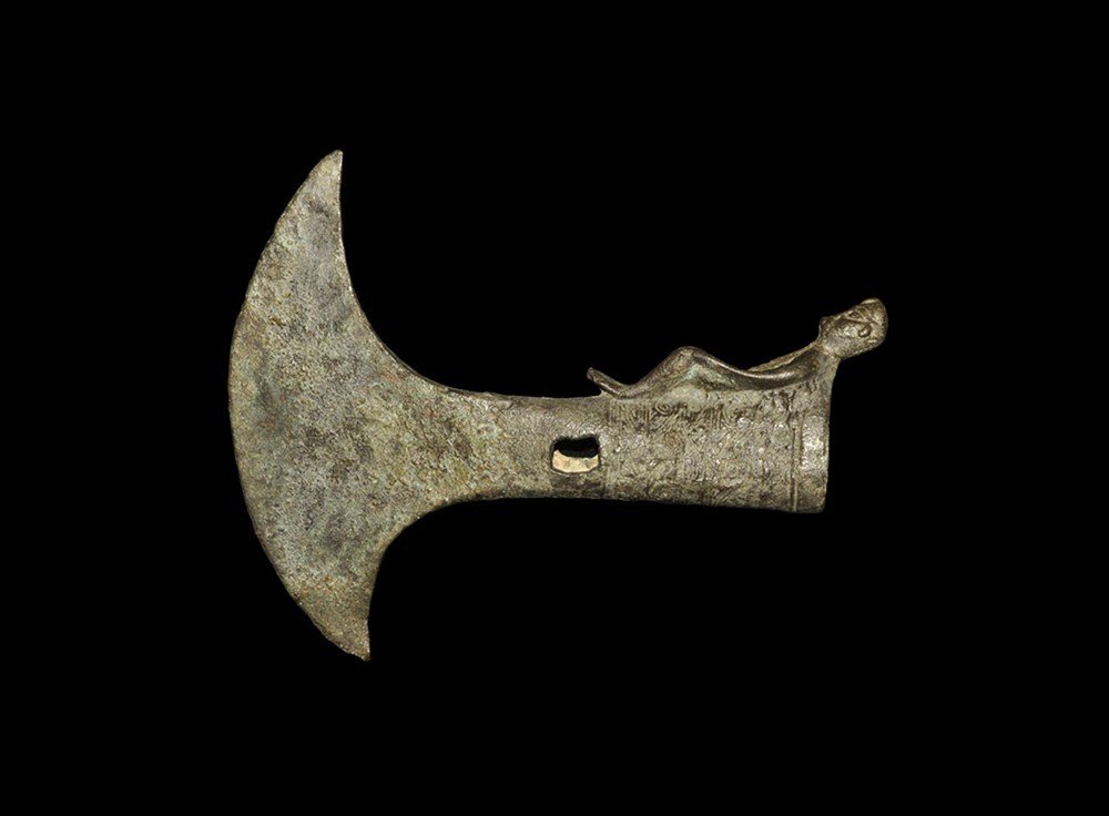 Chinese Style Bronze Axe Head: An undated archaisticcast axe-head with elliptical-section socket, pierced at the narrow end, expanding to an eccentric crescentic blade; bands of hatched texture to the socket and stamped text below;