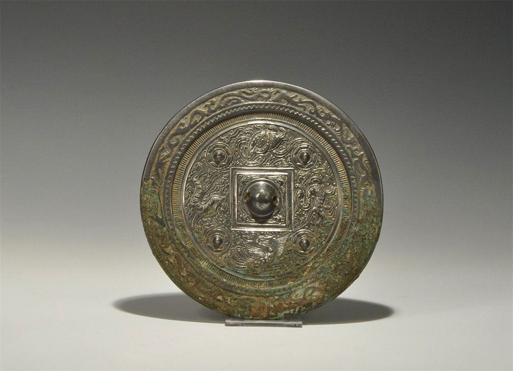 Chinese Style Tinned Bronze lion, Tortoise, Snake, Phoe: An undated archaistic cast-bronze disc mirror with one tinned and polished surface; to the reverse, a central pierced domed lug with surrounding square and band of scrolled foliage with lion, tortoise