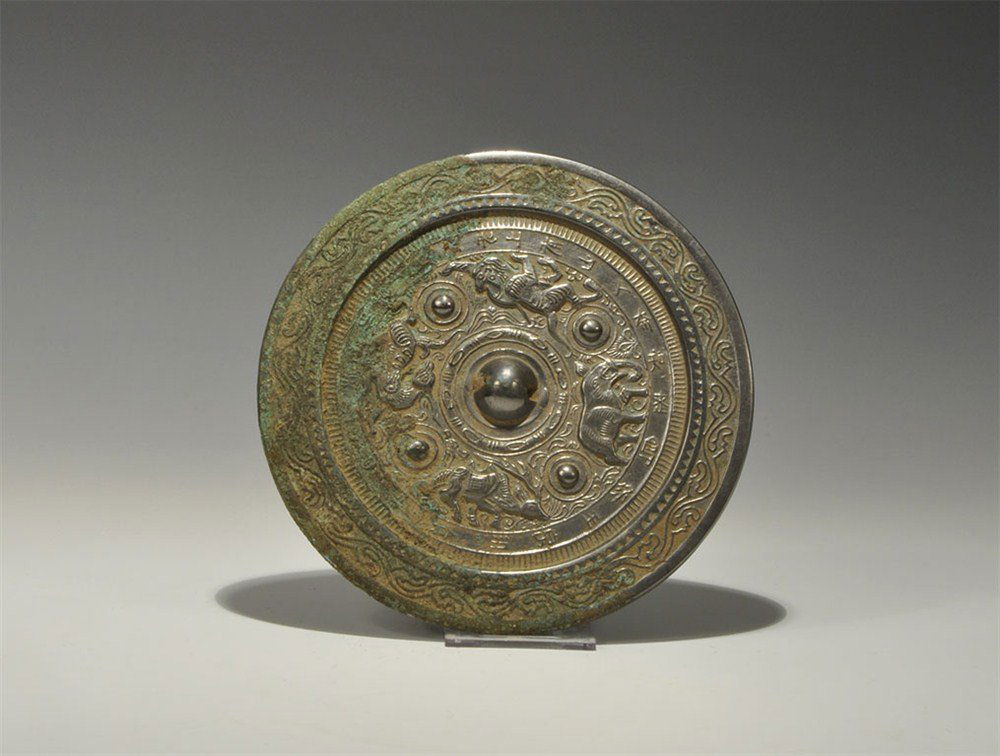 Chinese Style Tinned Bronze Elephant, Lion, Griffin and: An undated archaistic cast-bronze disc mirror with one tinned and polished surface; to the reverse, a central pierced domed lug with concentric bands of scrolled foliage with an elephant, lion, griffi