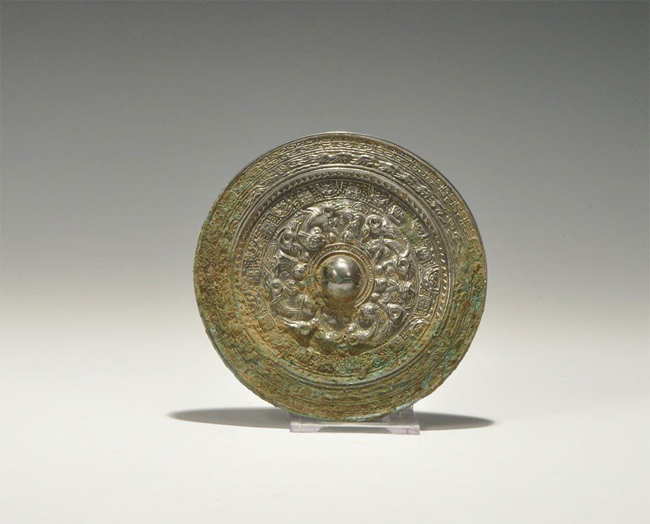 Chinese Style Tinned Bronze Birds and Geometric Motifs : An undated archaistic small cast-bronze disc mirror with one tinned and polished surface; to the reverse, a central pierced domed lug with concentric bands of birds and geometric motifs; to the rim an
