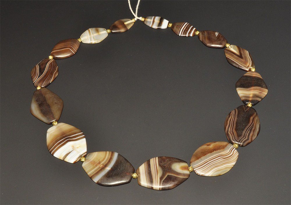Near Eastern Style Gold and Agate Bead String: An undated group of banded agate flat beads, lozengiform in plan, with gold seed bead spacers. Stone, 106 grams, 55 cm (21 1/2"). Acquired on the London art market in the 1960's.