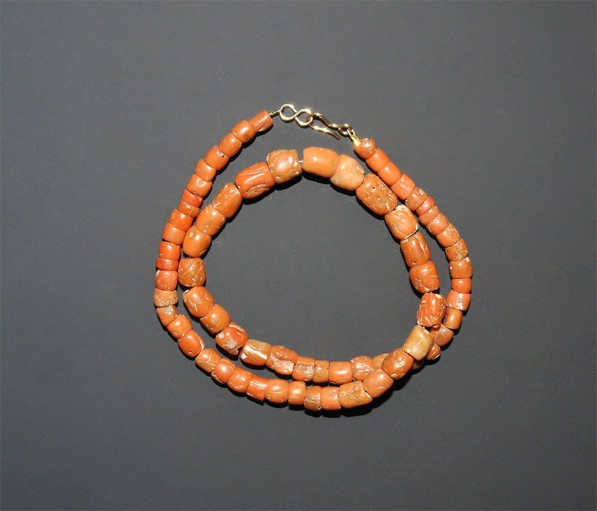 African Tribal Coral Bead Necklace: An old undated restrung necklace of seventy undated graduated natural orange coral beads, barrel shaped; Mediterranean workmanship; modern clasp. 31 grams, 42.5 cm (16 3/4"). From a London collection.