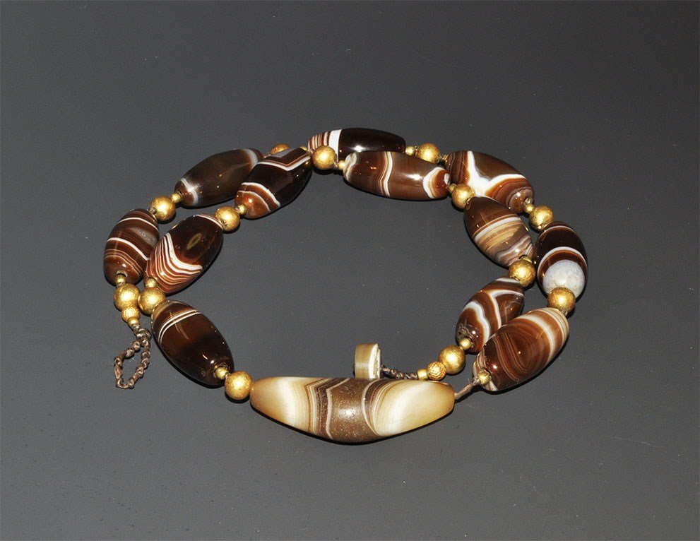 Islamic Persian Style Agate and Gold Necklace: An undated restrung necklace comprising nine fusiform and eleven oblate beads from Idar-Oberstein, with yellow metal seed bead spacers; the clasp an agate button and cord loop. 97 grams, 62 cm (24 1/2