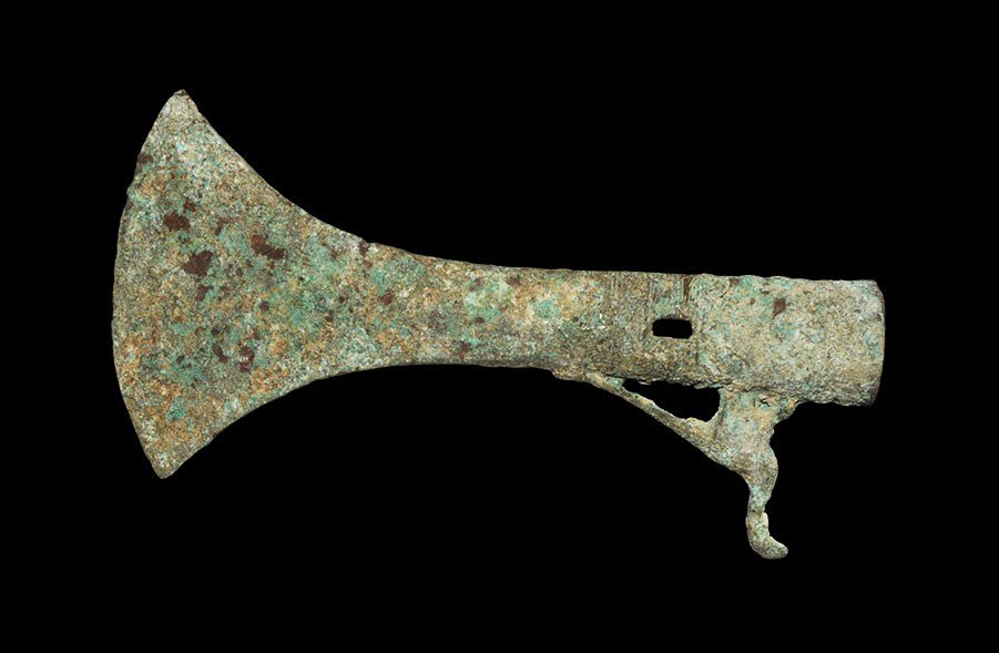 Chinese Zhou Bronze Axehead: Zhou Dynasty 1046–256 BC. A cast bronze axehead with elliptical-section socket and flared peltoid blade; the socket pierced to both faces for attachment; the upper edge of the socket ornamented with