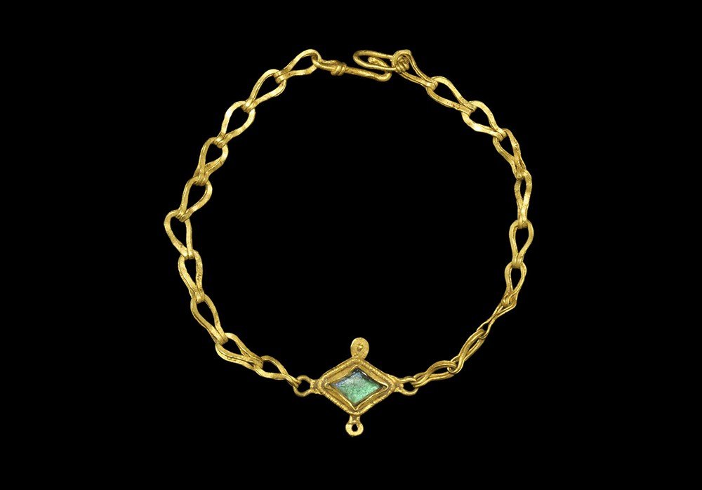 Roman Gold Bracelet with Green Stone: 3rd century AD. A gold bracelet formed as two lengths of doubled loop chain attached to a lozengiform plate with gold loop and granule details to the edges, filigree border and inset green hardstone i