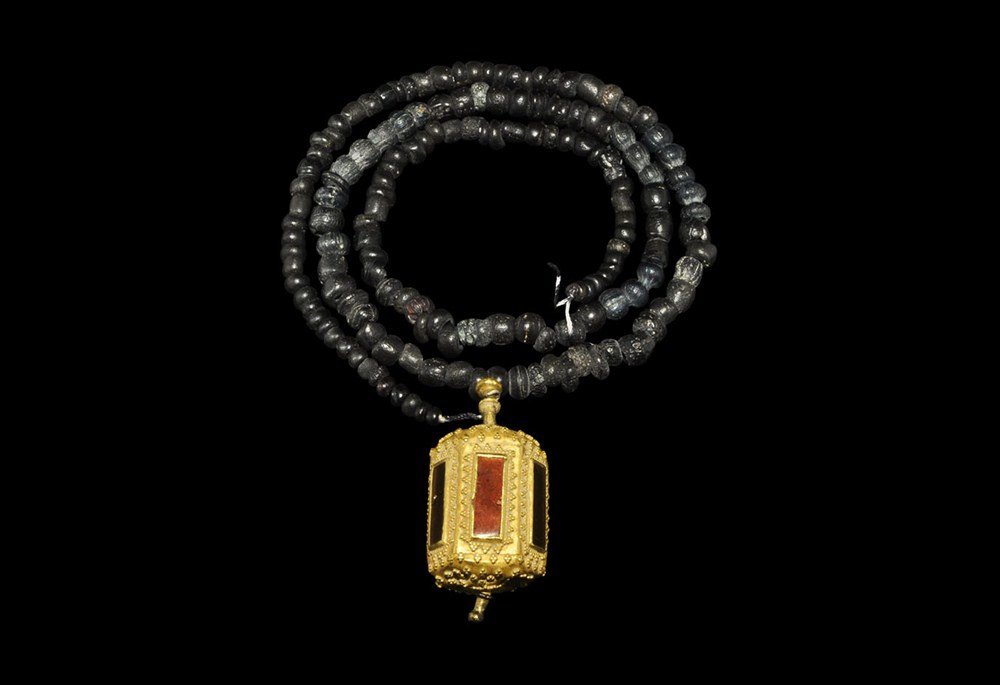 Byzantine Gold and Garnet Cylinder Pendant: 7th-8th century AD. A hollow sheet gold pendant, hexagonal in section with granulated surface, to each face a cloisonne garnet in a rectangular frame; supplied with a black hardstone seed bead necklac