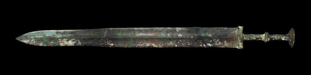 Chinese Bronze Sword: Han Dynasty, 206 BC-220 AD. A cast bronze sword, the blade triangular with thick central rib; the guard elliptical in section with thin ribbed round-section grip and slightly dished disc pommel. 738 g