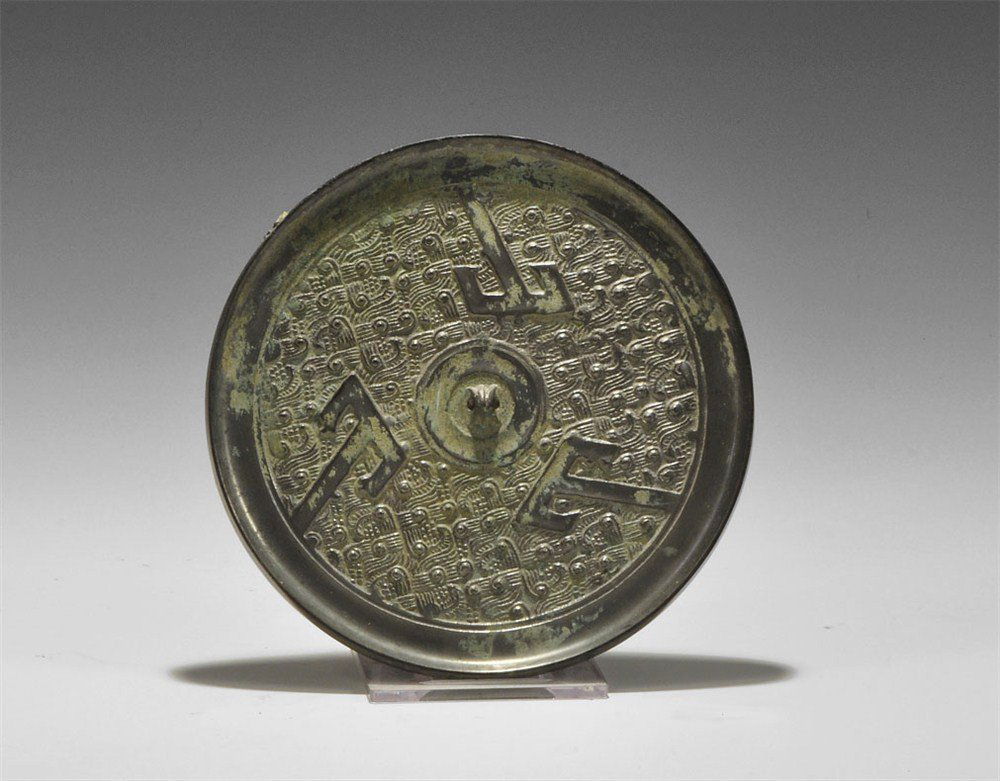 Chinese Bronzed Tinned Hand-Mirror: Tang Dynasty, 618-906 AD.. A cast bronze mirror with one tinned surface; to the reverse a pierced lug surrounded by three T-shaped motifs on a geometric background. 274 grams, 12.5 cm (5"). Ex McQuinl