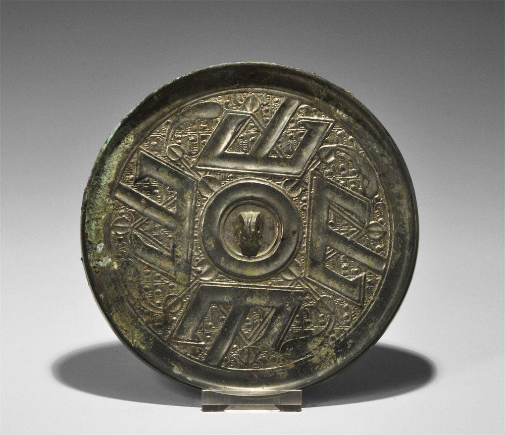 Chinese Bronzed Tinned Hand-Mirror: Tang Dynasty, 618-906 AD. A cast bronze mirror with one tinned surface; to the reverse a pierced lug surrounded by four T-shaped motifs on a geometric background. 787 grams, 19 cm (7 1/2"). Ex McQuinl