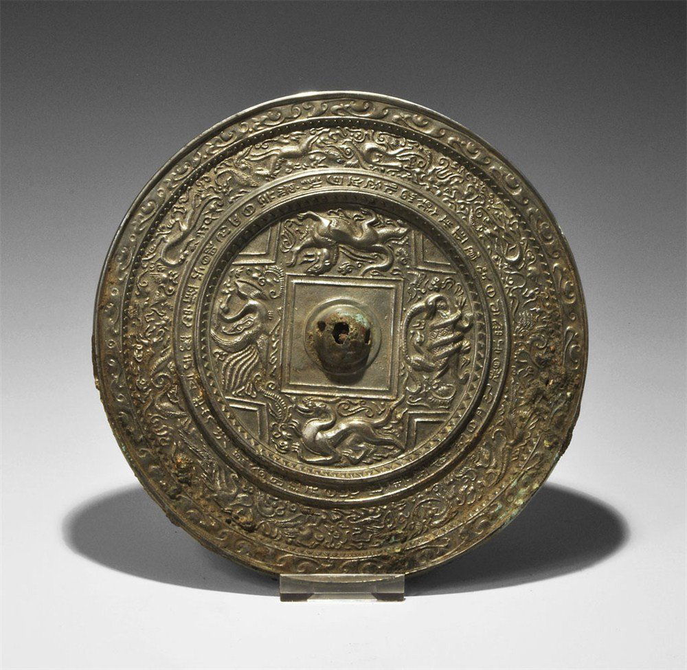 Chinese Bronzed Tinned Epigraphic Hand-Mirror: Tang Dynasty, 618-906 AD. A cast bronze mirror with one tinned surface, the reverse decorated with a central pierced lug and band of animals and birds amid scrolls, and outer frieze of similar motifs