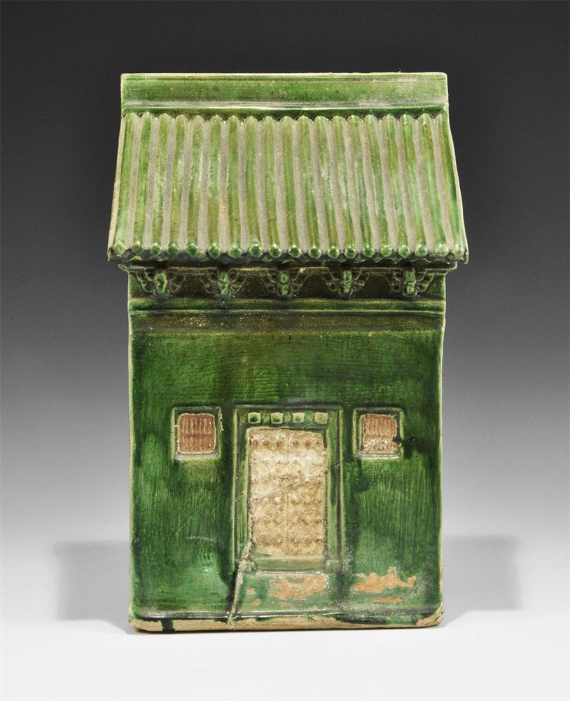 Chinese Glazed 'House' Shrine: Ming dynasty, 1450-1600 AD. A hollow ceramic shrine in the form of a house with pitched roof, door and small side windows, green-glazed to the main face, two circular lateral holes and two more to the
