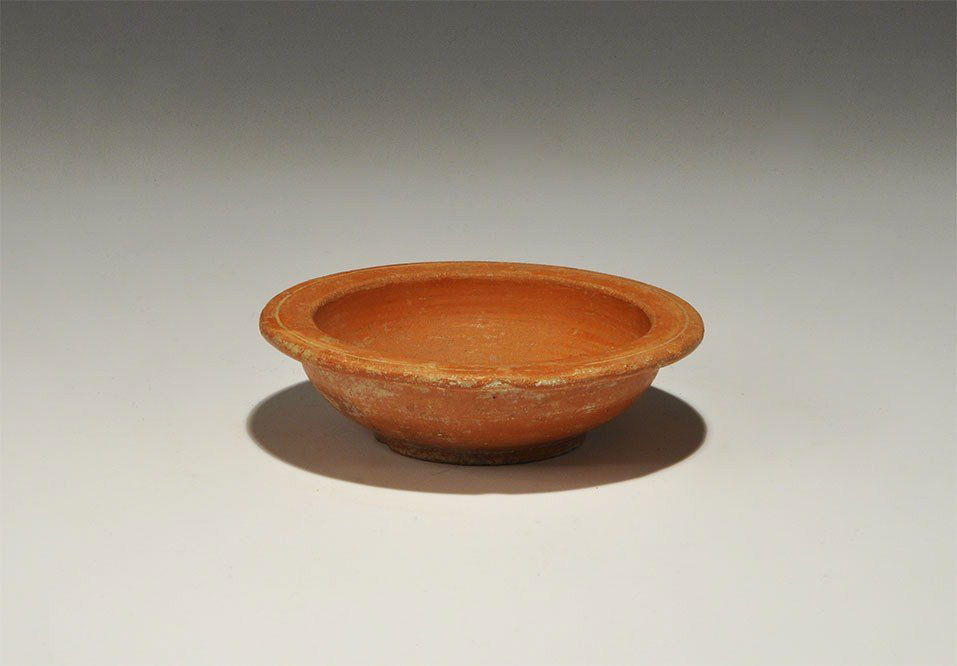 Roman Ceramic Redware Bowl: 1st-3rd century AD. A low bowl with basal ring and flanged rim, a single incised line to the rim, hemispherical bpdy; the fabric a glossy orange-red of terra sigillata type. 119 grams, 11.5 cm (4 1/2"