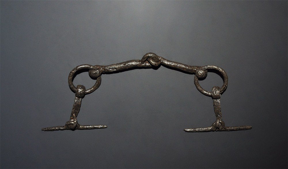 Medieval Iron Horse Curb Bit: 14th century AD. A hand-forged iron curb bit of Ward-Perkins's type II with free-running rings to the cheeks, articulated central joint; the recurved joints forged shut, the rings round-section; from