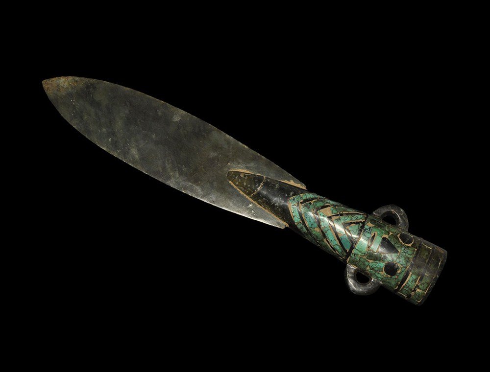 Central American Style 'Jade' Dagger with Inlaid Turquo: An undated stone leaf-shaped dagger with conical hilt inlaid with turquoise panels representing a human face and body with crossover coat, c-shaped lugs to the sides. 967 grams, 40 cm (15 3/4"). Prope