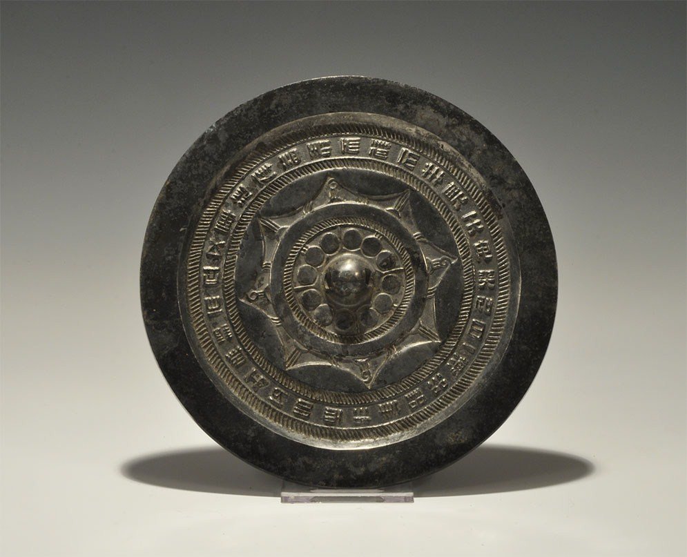 Chinese Han Style Bronze Mirror: A n undated archaistic cast disc mirror in tin-rich bronze with one reflective surface; to the reverse a central pierced hub and rosette, surrounding band of text within hatched zone. 752 grams, 18 cm