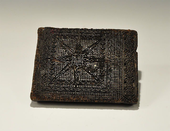 Islamic Wooden Clothes Stamp: 19th century AD. A carved wooden block with chamfered handle to the upper face, five longitudinal piercings; the stamp face with densely-carved surface design comprising a central cross and eight radi