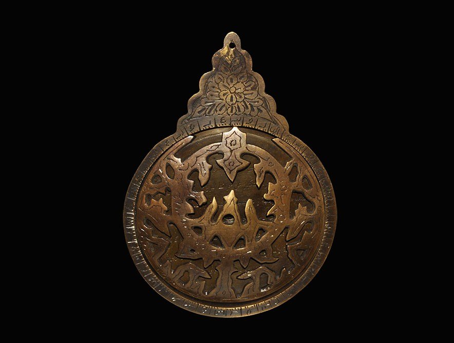 Islamic Bronze Astrolabe: An undated archaistic astrolabe comprising a hollow discoid plate with recess to the upper face and sub-triangular suspension plate above with rosette detail; the edge with graded scale, the inner fac