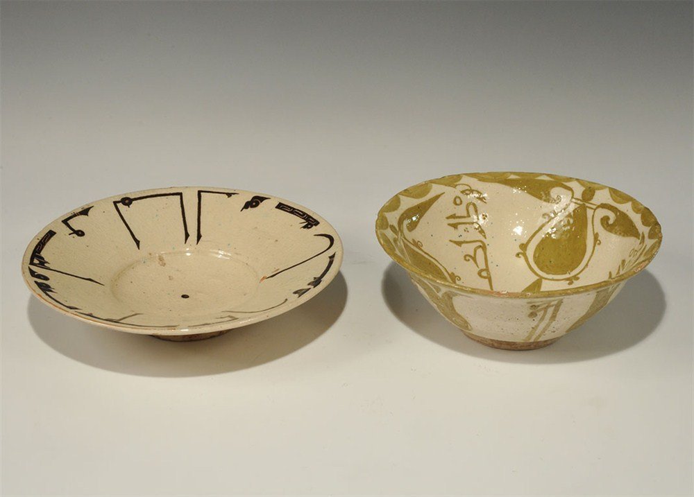 Islamic Korosan Style Glazed Ceramic Bowl Group: A mixed group of undated archaistic cream-glazed ceramic vessels comprising: one with carinated underside, concave inner face with central recess, band of black calligraphic text to the rim; one with 