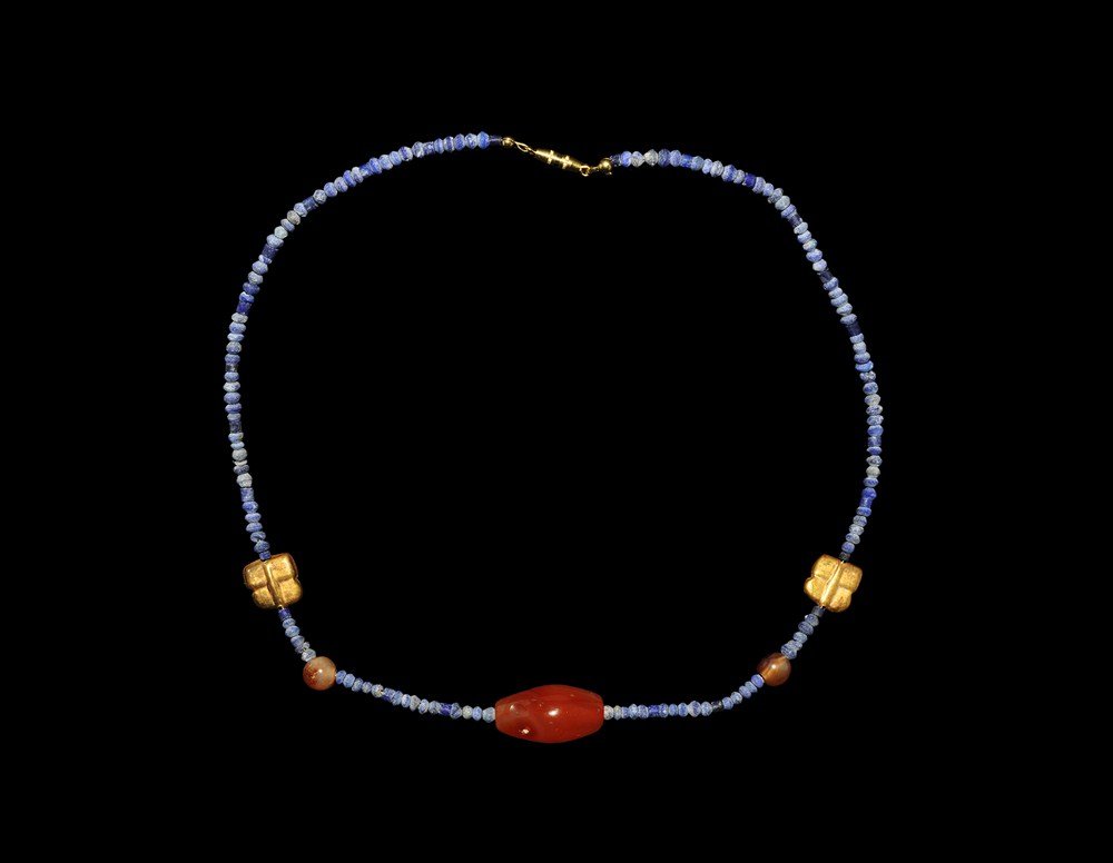 Near Eastern Bactrian Gold, Lapis Lazuli and Carnelian : 1st millennium BC and later . A restrung necklace comprising small carved drilled lapis beads from Afghanistan, featuring two square-shaped gold beads, two carnelian spherical beads, one oval carnelia