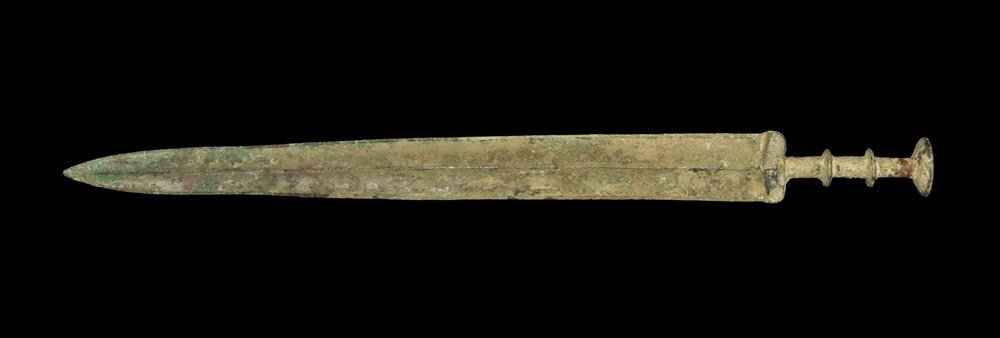 Chinese Bronze Sword: Han Dynasty, 206 BC-220 AD . A cast sword, the blade slightly waisted with central rib; the guard elliptical in section with thin ribbed round-section grip and dished disc pommel. 756 grams, 56 cm (22