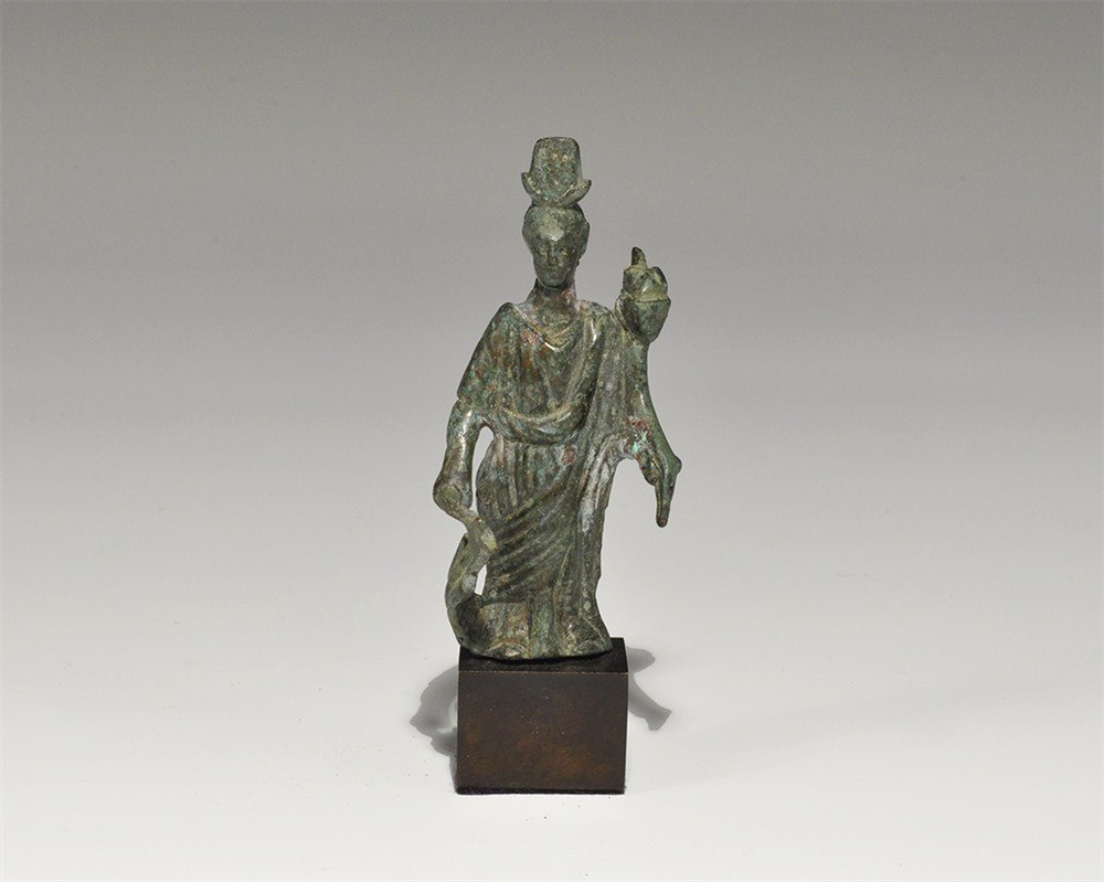 Roman Bronze Isis Fortuna Statuette: 1st-2nd century AD . A cast statuette of the goddess Isis Fortuna standing robed with a ship's rudder in her right hand and cornucopia in her left, a headdress of horns and feathers; mounted on a cust