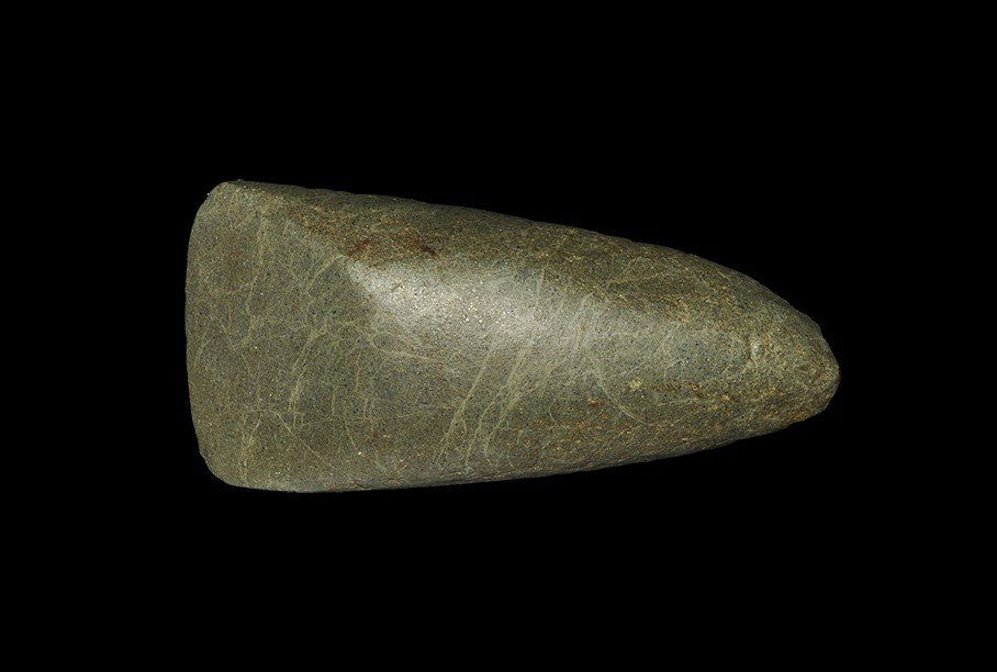 Stone Age Greenstone Polished Adze: Neolithic period, 4000-2000 BC . A polished stone adze of triangular form with rounded butt, round in general section with chamfered, slightly convex cutting edge; in a veined greenstone. 430 grams, 1