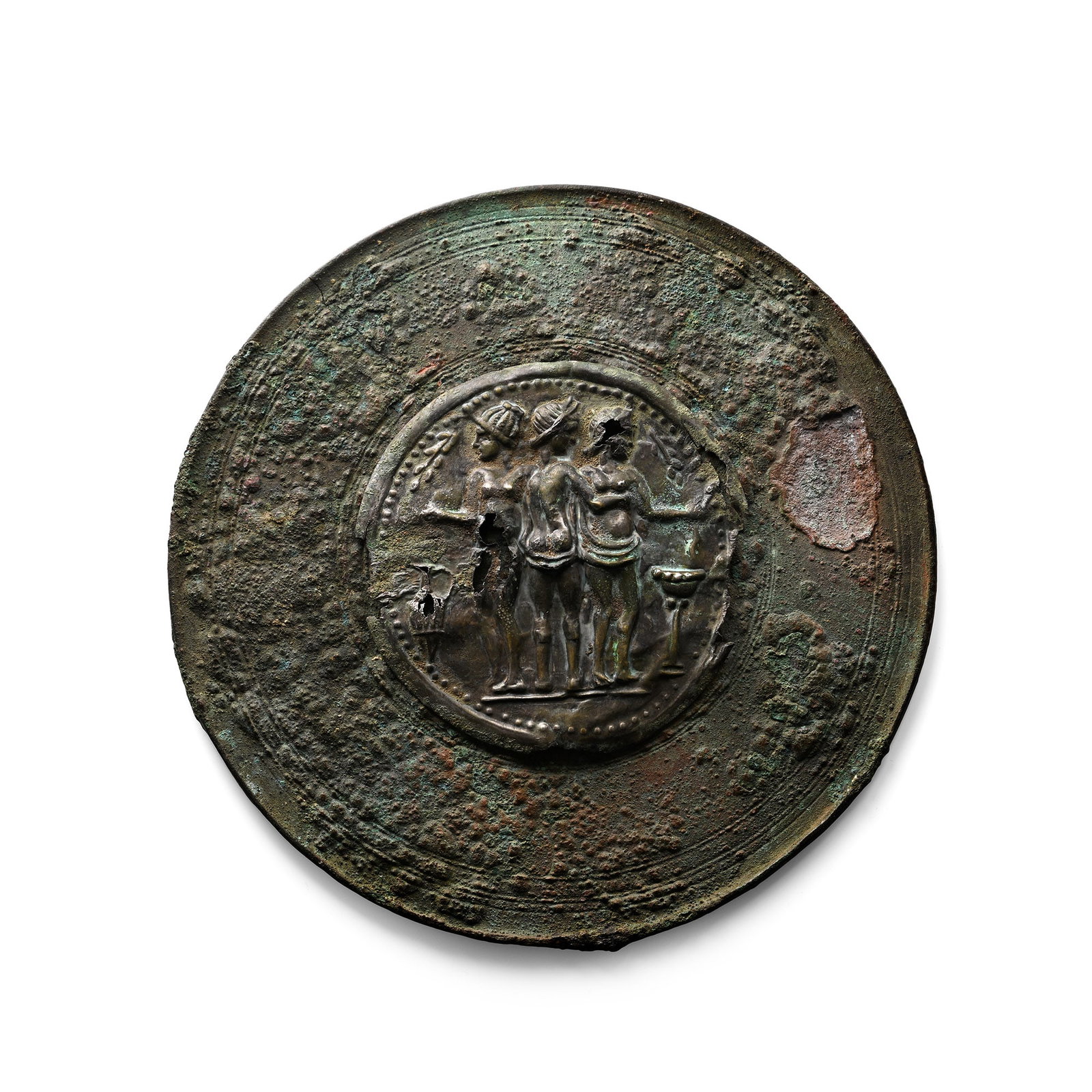 Large Roman Bronze Mirror with Three Graces Silver Plaque: 1st-4th century A.D. Discoid in plan with raised rim and concentric rings; central applied sheet-silver plaque with three standing females between a jug and a bowl, each on a stand; pelletted rim. 497