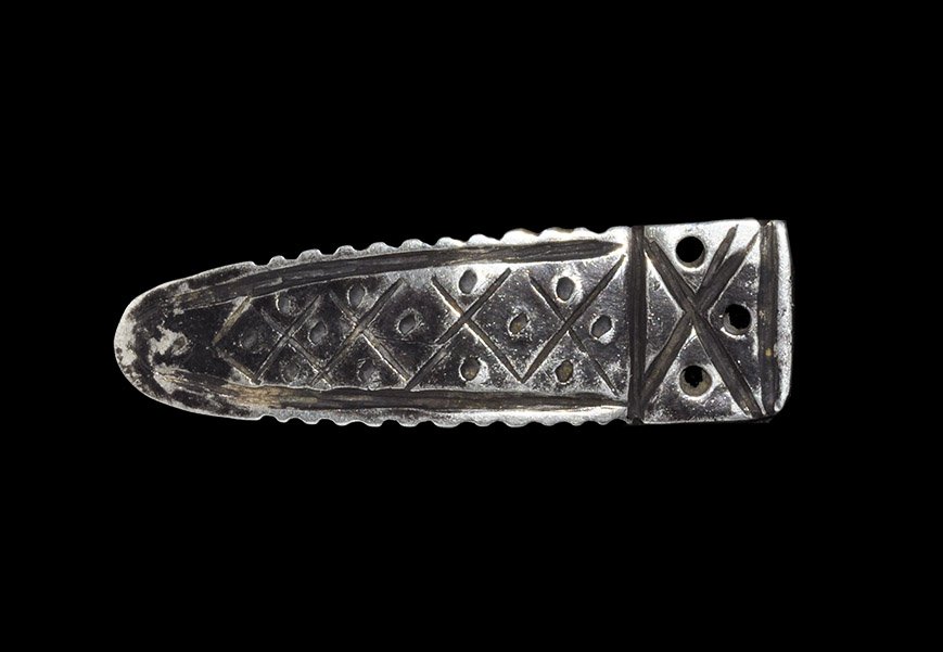 Medieval Silver Strap-End: 13th-15th century AD. A cast tongue-shaped strap end with rilled edge, lozenge and punched dot motifs to the upper face, saltire and three holes to the upper end, two convergent bands to the reverse. 