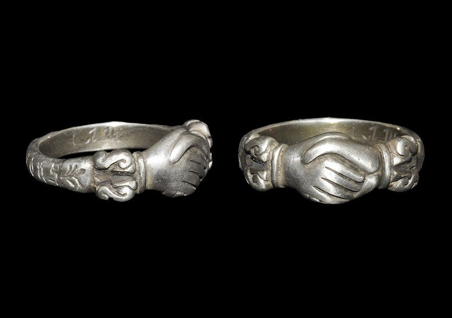 Post Medieval Tudor Style Silver Inscribed Fede Ring: An undated fede finger ring with clasped hands motif modelled in the half-round and scrolled cuffs; to the outer face of the hoop the text in a bastarde hand 'ie vend de vous' (I depend on you?). Priv