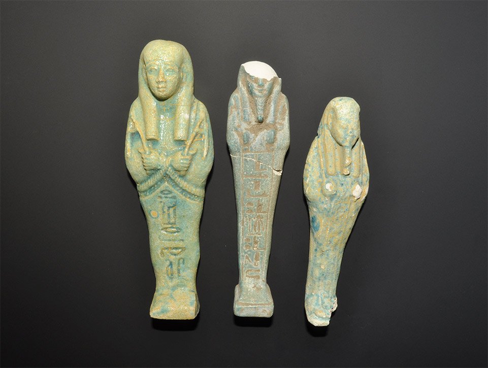 Egyptian Style Glazed Composition Shabti Group: A mixed group of undated archaistic glazed composition shabtis comprising: one with tripartite wig and plaited beard; one similar with dorsal pillar and hieroglyphic text to the lower body; one with t