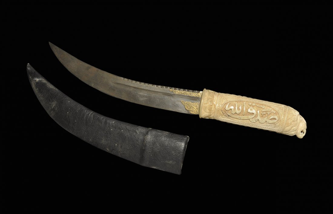 Islamic Indian Style Dagger: An undated archaistic dagger with composition hilt and curved blade; the hilt with calligraphic text ornament to the sides, lion-head terminal; the blade with inlaid arabesque motif to each face; with