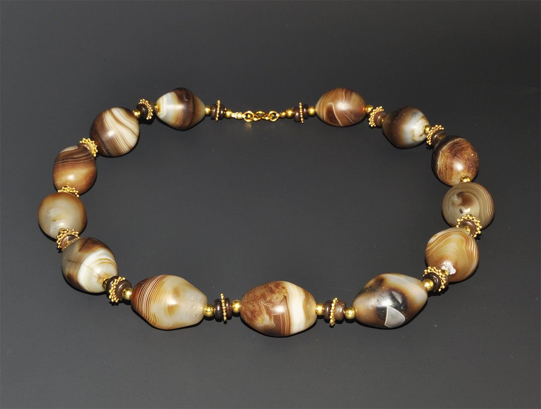Bactrian Style Banded Agate Bead Necklace: An undated restrung necklace of brown-cream oval banded agates with small gold rosettes, gold beads and discs between. Acquired on the London art market in the 1960s. 232 grams, 56 cm (22"). [No Reser
