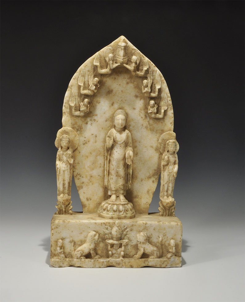 Chinese Style Stone Buddha Altar: An undated archaistic carved marble altar with rectangular base and ovoid backplate; the central figure depicting the Buddha standing on a lotus bloom with his hands in the gestures of charity and pro
