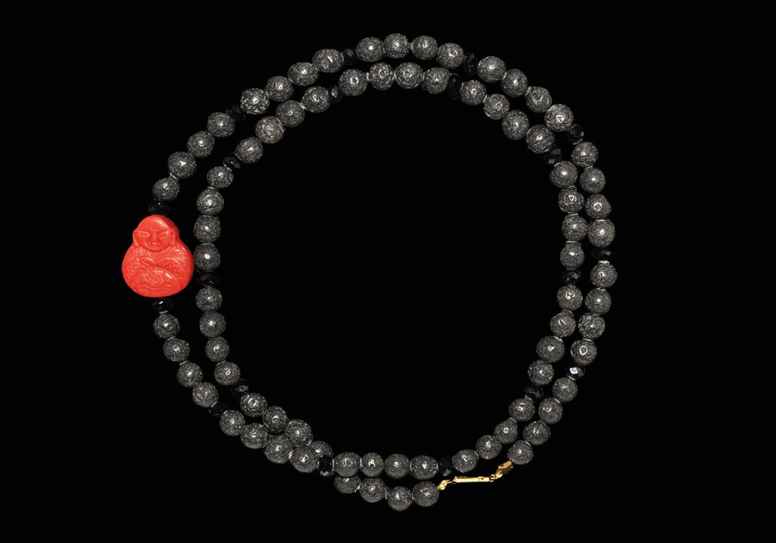 Chinese Cinnabar Buddha and Lava Bead Necklace: A restrung group of undated archaistic designer necklace of “Lava” or “Tufa” beads, moulded cinnabar centre bead, faceted black glass“jet” beads. From a Middlesex collection. 118 grams, 96