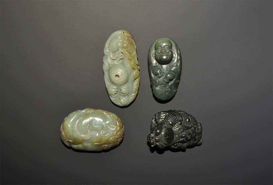 Chinese Style Stone Pendant Group: A mixed group of undated archaistic carved stone pendants comprising: one elliptical with fish and waves motif; one a toad wit a string of coins on its back; one a figure of the Buddha, smiling; one e