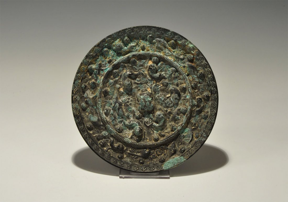 Chinese Style Bronze Figural Mirror: An undated archaistic small cast-bronze disc mirror with one tinned and polished surface; to the reverse, a central pierced monkey-shaped lug with concentric bands of scrolled foliage with monkeys and