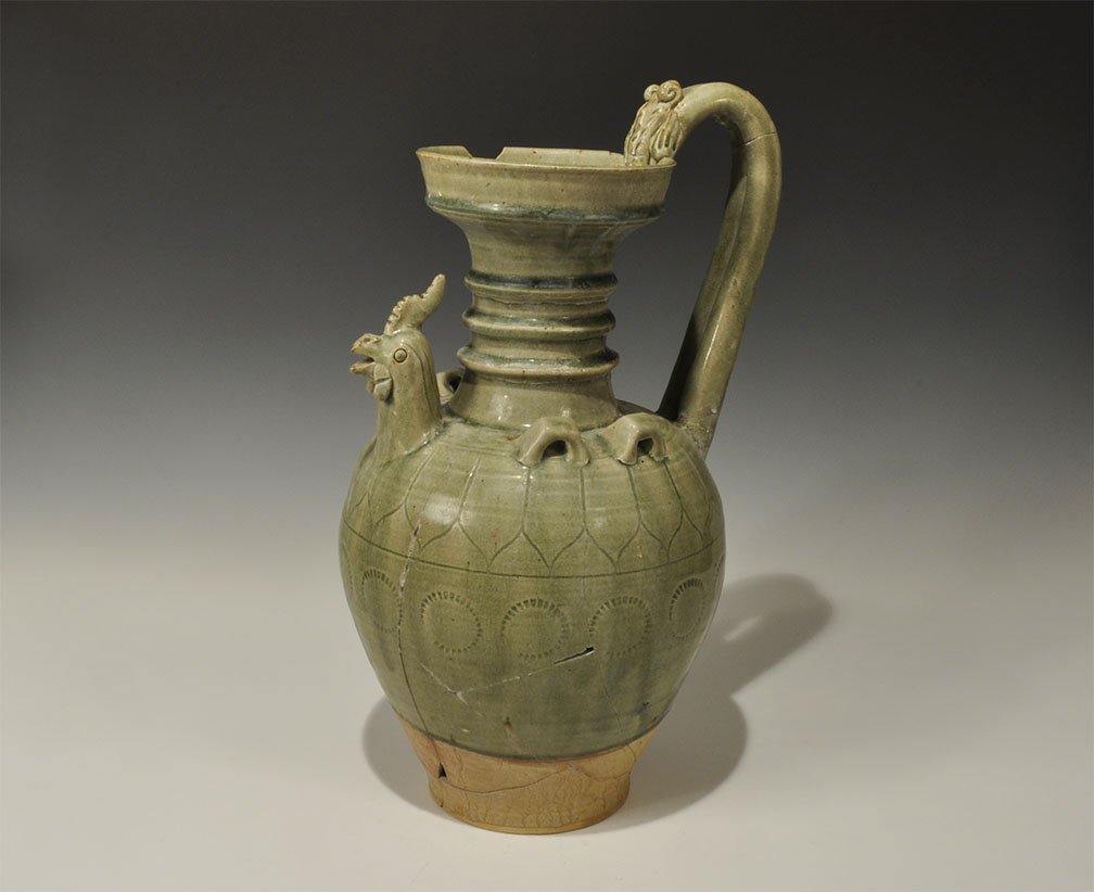 Cambodian Style Green-Glazed Ceramic Cockerel Jug: An undated archaistic green-glazed ceramic jug, bulbous in profile with tall ribbed neck and recessed rim, round-section handle with beast-head finial to the rear; to each side a pair of square lugs w